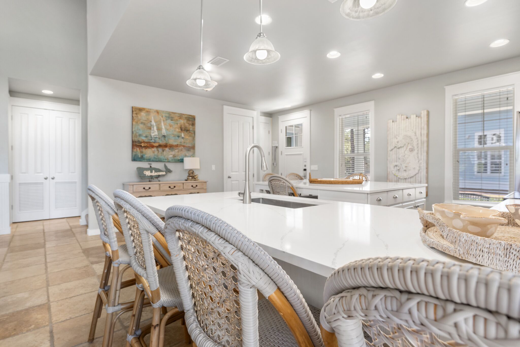 A modern kitchen with a large island, white cabinetry, and wicker chairs.