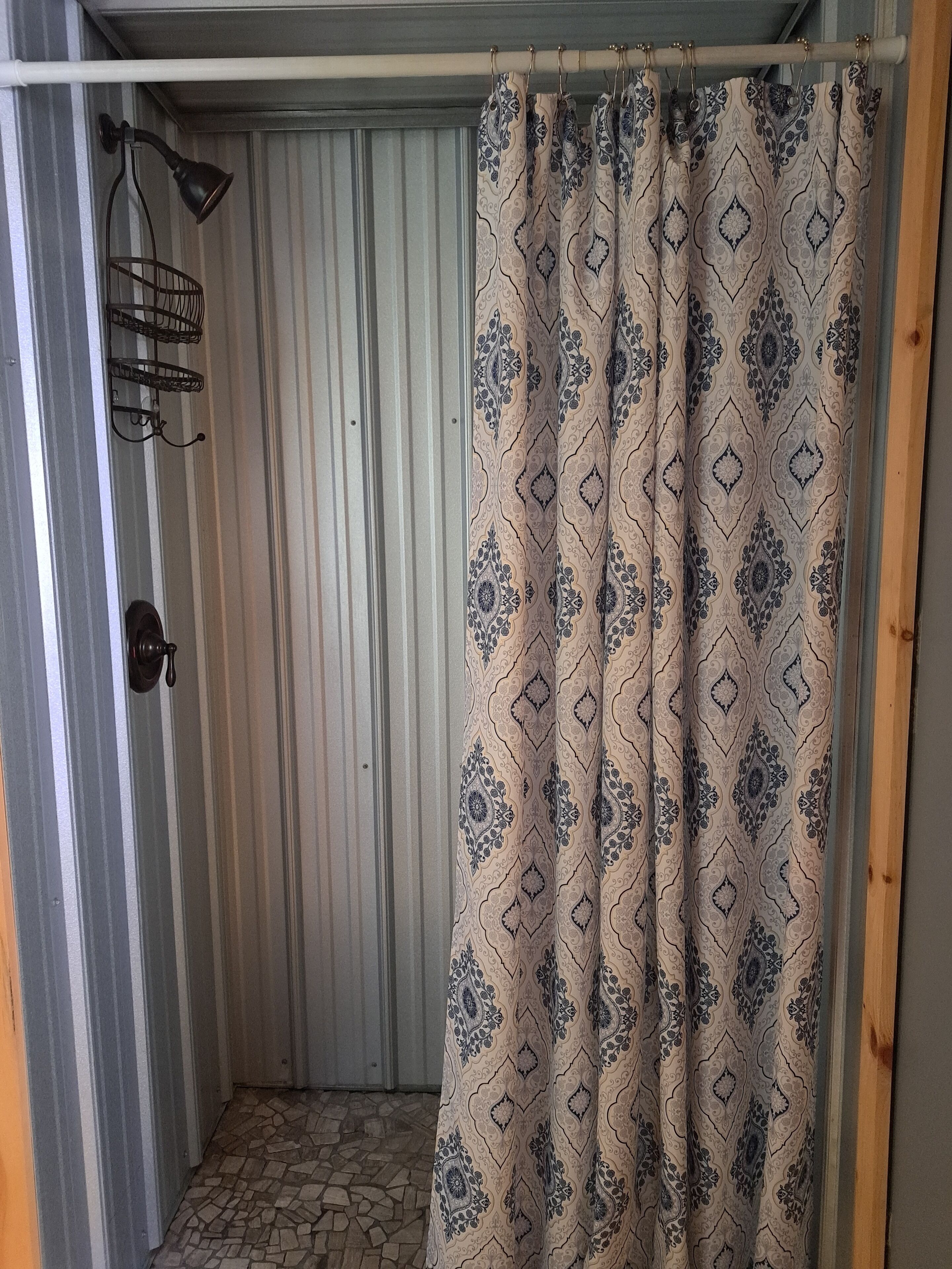 A shower area with a patterned shower curtain, a metal rack, and a door with a handle.