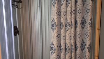 A shower area with a patterned shower curtain, a metal rack, and a door with a handle.