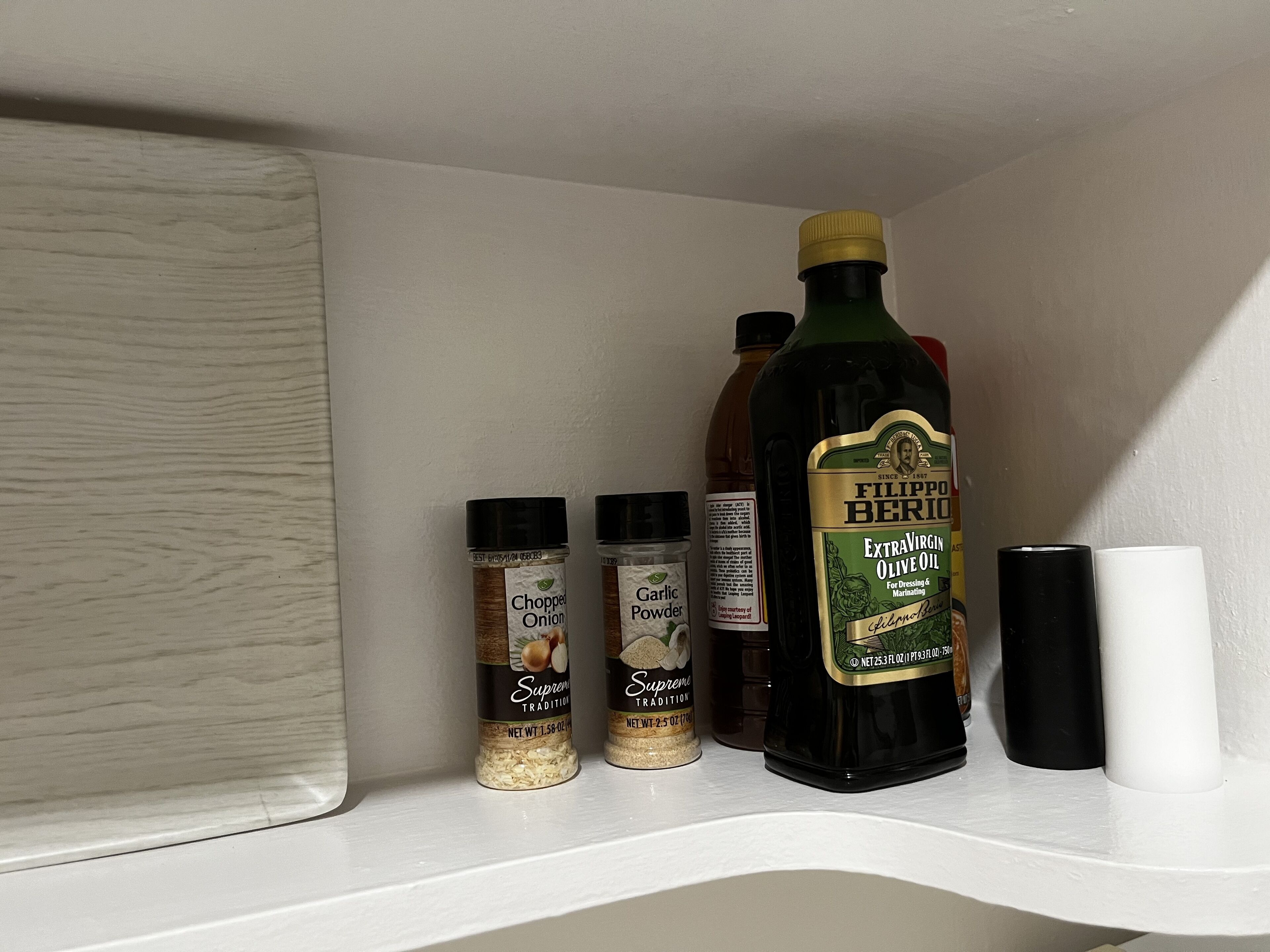 Une étagère contenant divers articles de cuisine, notamment des bouteilles d’huile d’olive, des oignons hachés et de la poudre d’ail.