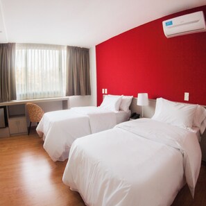 Habitación de hotel con dos camas, un escritorio y una ventana con cortinas.