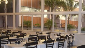 Un restaurante con varias mesas dispuestas para comer, ventanas amplias y plantas de interior.