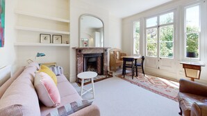 Un salón con chimenea, sofá, sillón, mesa y ventana con vistas a follaje.