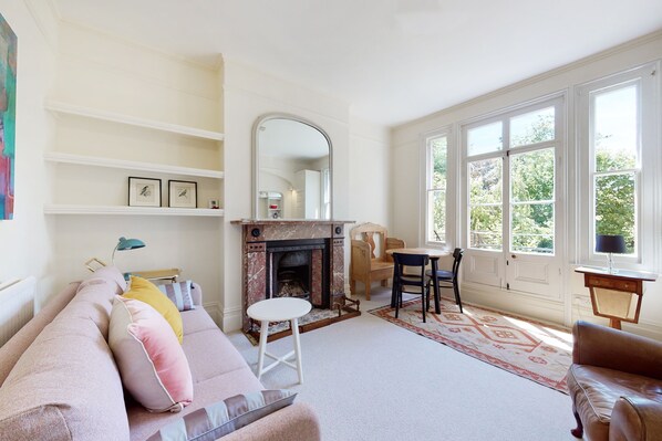 A living room with a fireplace, a sofa, a chair, a table, and a window with a view of greenery.