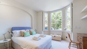 Un dormitorio con una cama grande, un escritorio, una silla y una ventana con contraventanas.