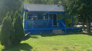 A small, colorful house with a blue and green exterior, a porch, and a lawn. - Charming 2-bedroom cottage by the water (Utterson)