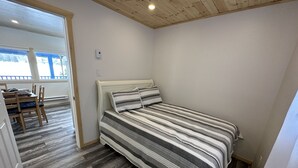 A bedroom with a bed, wooden floor, and a view of an outdoor balcony. - Charming 2-bedroom cottage by the water (Utterson)