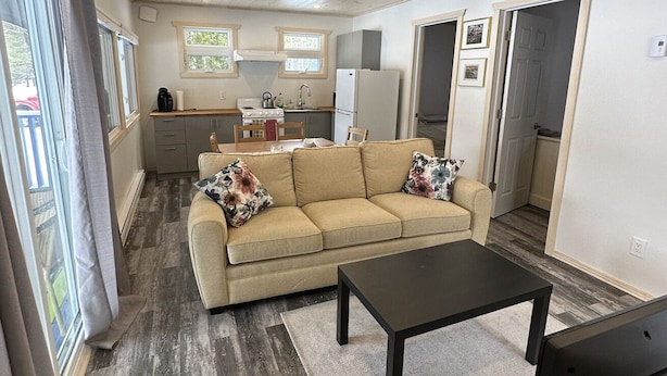 A cozy living room with a sofa, a coffee table, and a TV. There is a kitchen area with a stove, sink, and refrigerator. - Charming 2-bedroom cottage by the water (Utterson)