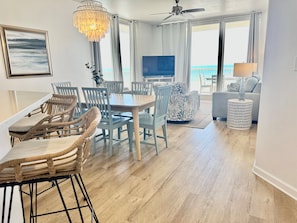 Un coin repas avec des chaises en osier, une table en bois, un lustre et un téléviseur en arrière-plan.