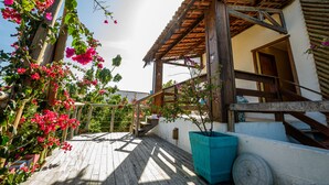 Una terraza de madera con una pérgola, una planta en maceta y una escalera que lleva a un edificio.