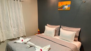 Una cama bien hecha con una colcha gris estampada, dos almohadas blancas y dos toallas con motivos florales rojos.