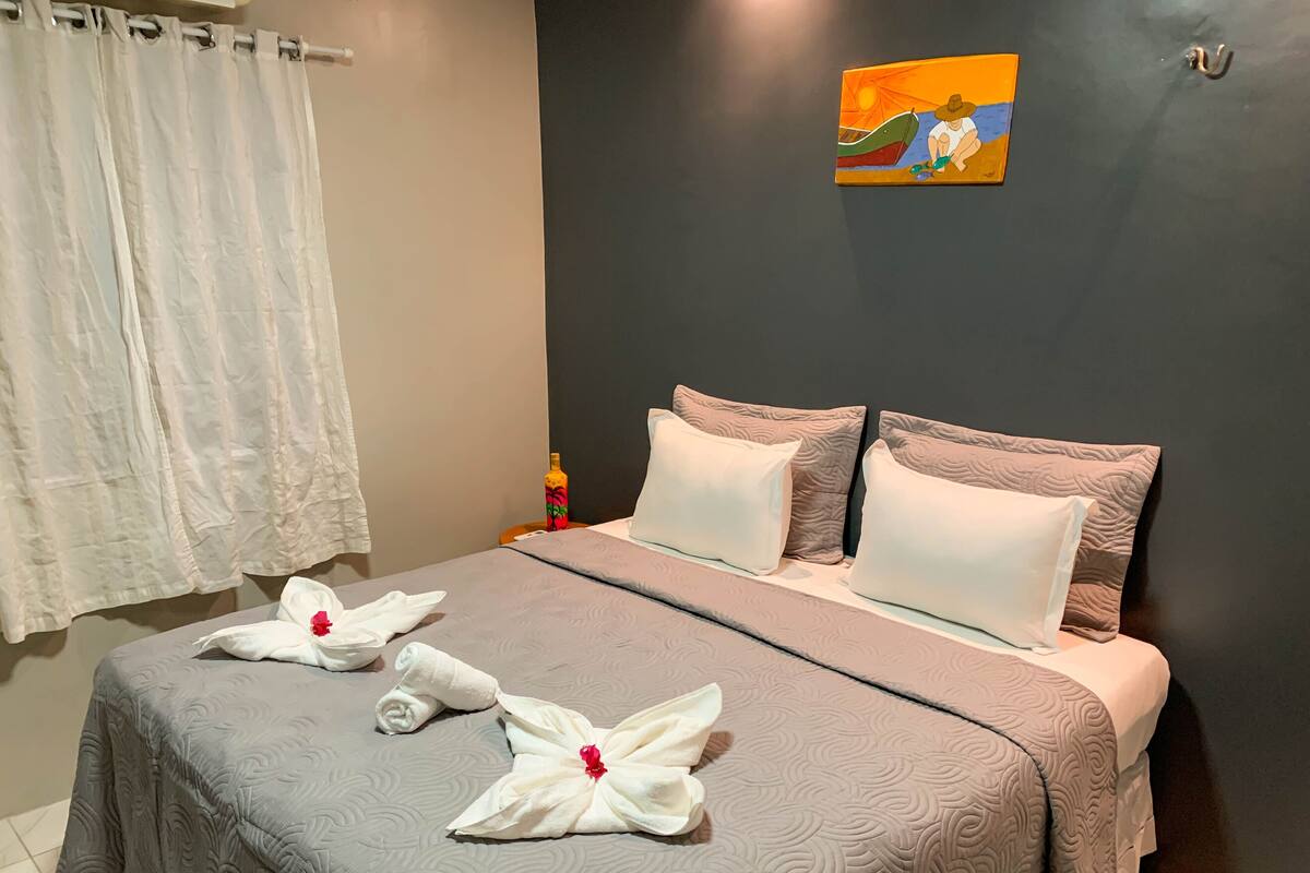 Una cama bien hecha con una colcha gris estampada, dos almohadas blancas y dos toallas con motivos florales rojos.