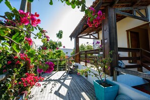 Eine Holzdar Terrasse mit einer Treppe zu einem überdachten Bereich, umgeben von blühenden rosa Blumen und Grünpflanzen.