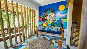 Una habitación con un piso de baldosas coloridas, un tapete tejido, un banco de madera y un mural en la pared.