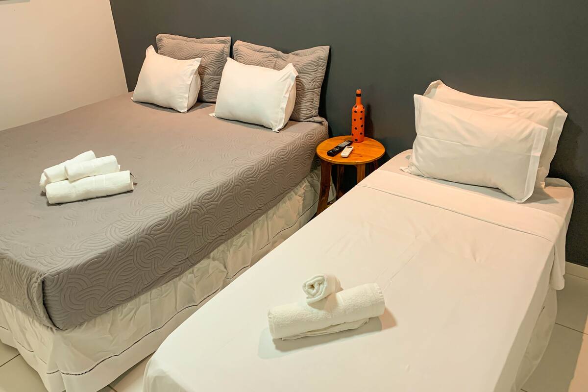 Una habitación de hotel con una cama grande, una cama más pequeña y una mesita de noche con un control remoto.