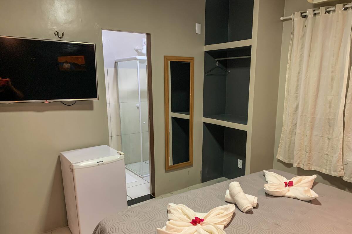 Habitación de hotel con cama, refrigerador pequeño, televisión montada en la pared, zona de ducha y espejo.