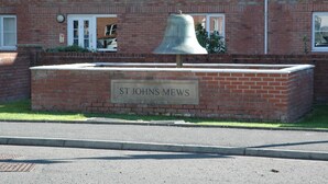 A brick building with a large bell in front and a sign that reads 'ST JOHNS MEWS'.