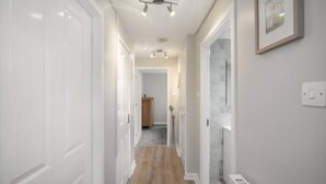 A hallway with white doors, a wooden floor, a ceiling fan, and a framed picture on the wall.