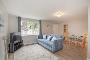 A living room with a sofa, TV, dining table, chairs, and a window.