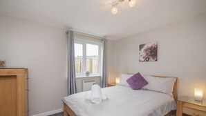 A bedroom with a bed, a bedside table, a window with curtains, a radiator, and a wall-mounted picture.