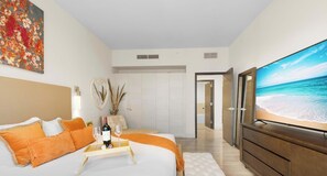 A bedroom with a bed, a bedside table with a bottle and glasses, a mirror, a wardrobe, and a painting on the wall.
