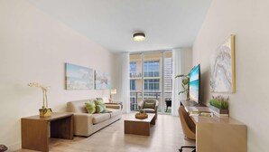A modern living room with a sofa, coffee table, and TV stand, large windows, and artwork on the walls. - Perfect Relax| Rooftop Pool+ Gym – Hot Tub (Hollywood)