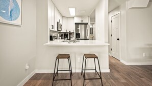 Une cuisine moderne avec un îlot central blanc, deux tabourets et des appareils électroménagers en acier inoxydable.