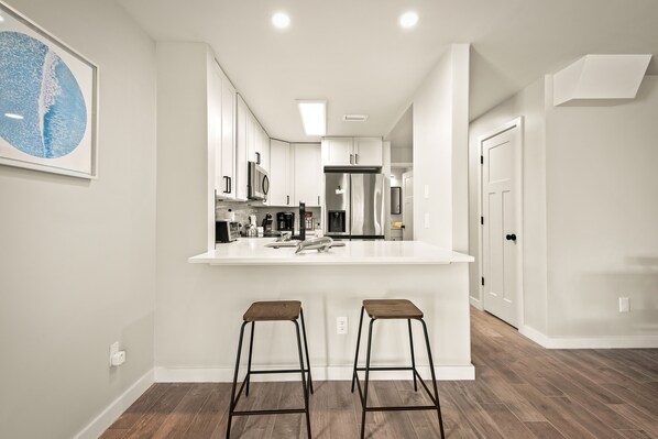 A modern kitchen with a white island, two stools, and stainless steel appliances.