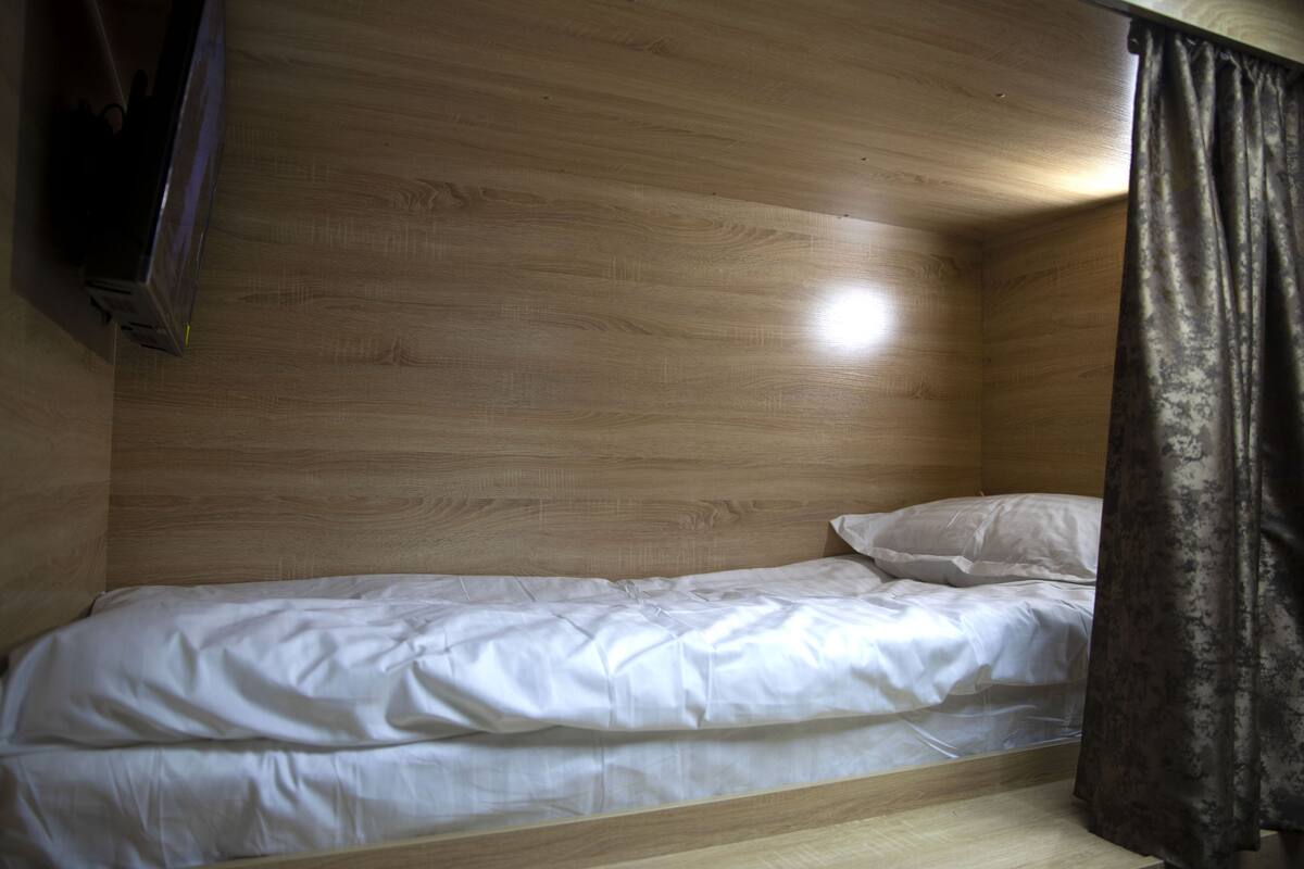 A single bed with white bedding in a room with wooden walls and a curtain on the right.