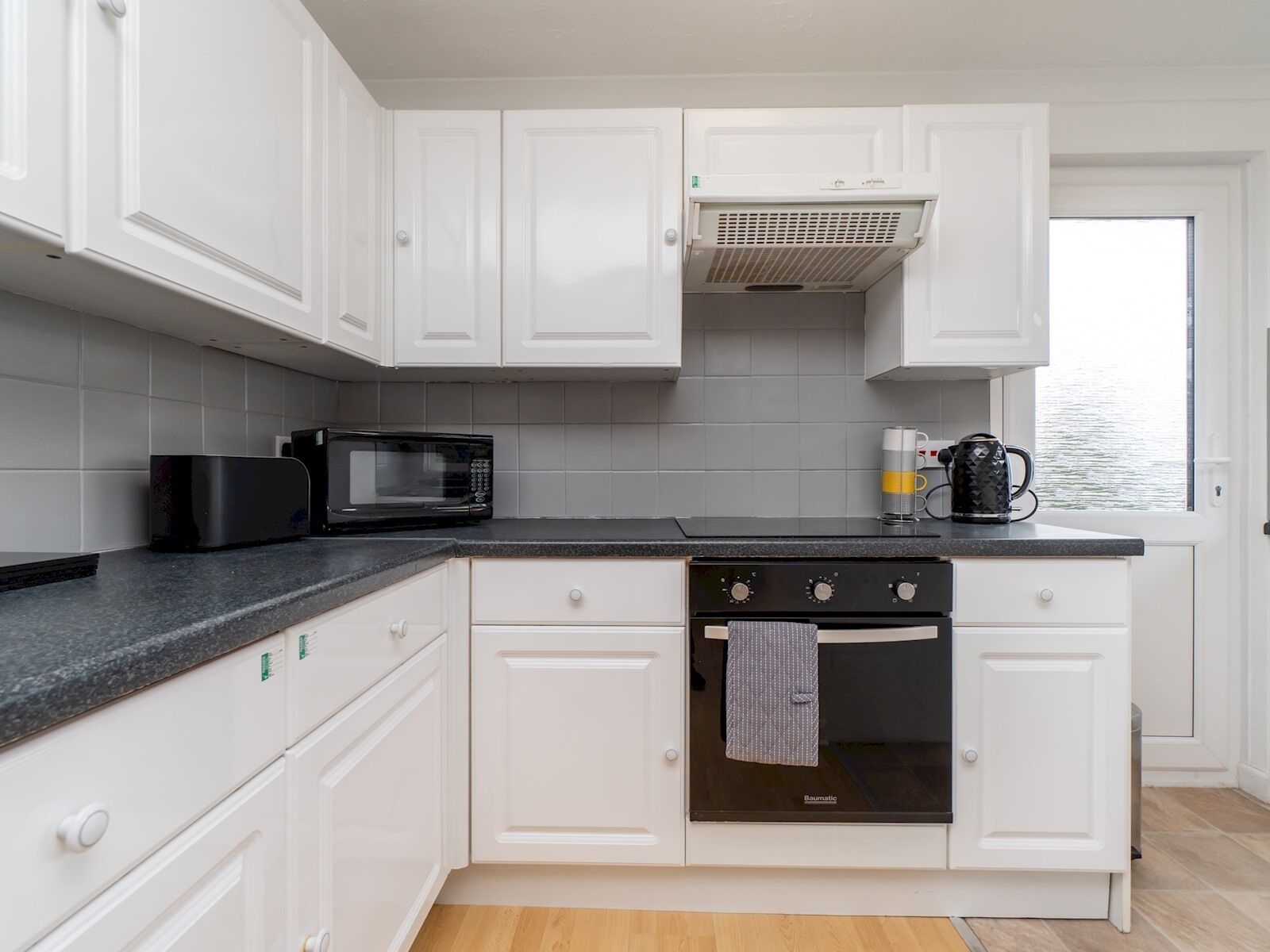 A kitchen with white cabinets, a black microwave, a stove, and a coffee maker.