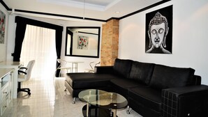 A modern living room with a black sectional sofa, a glass coffee table, a white desk, and a black-framed picture of a Buddha. - 1 bed Condo Jomtien Beach (Pattaya)