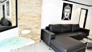 A modern living room with a sectional sofa, a glass table, and a brick accent wall. - 1 bed Condo Jomtien Beach (Pattaya)