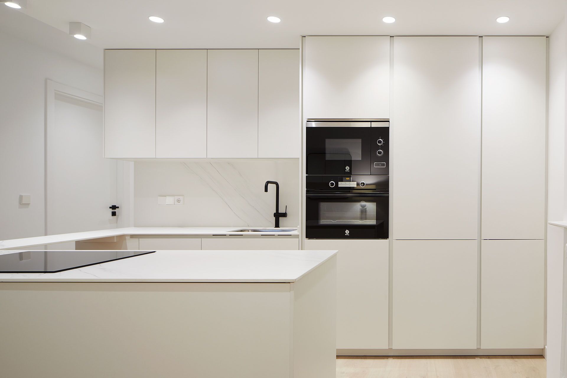 Une cuisine moderne avec des meubles blancs, un four encastré noir et un élégant plan de travail noir.