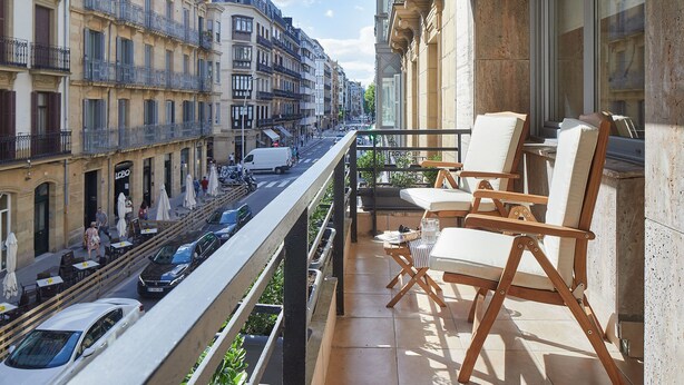 A balcony with outdoor furniture, overlooking a street with parked cars and buildings.