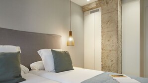 A modern hotel room with a large bed, a hanging light fixture, and a concrete accent wall.
