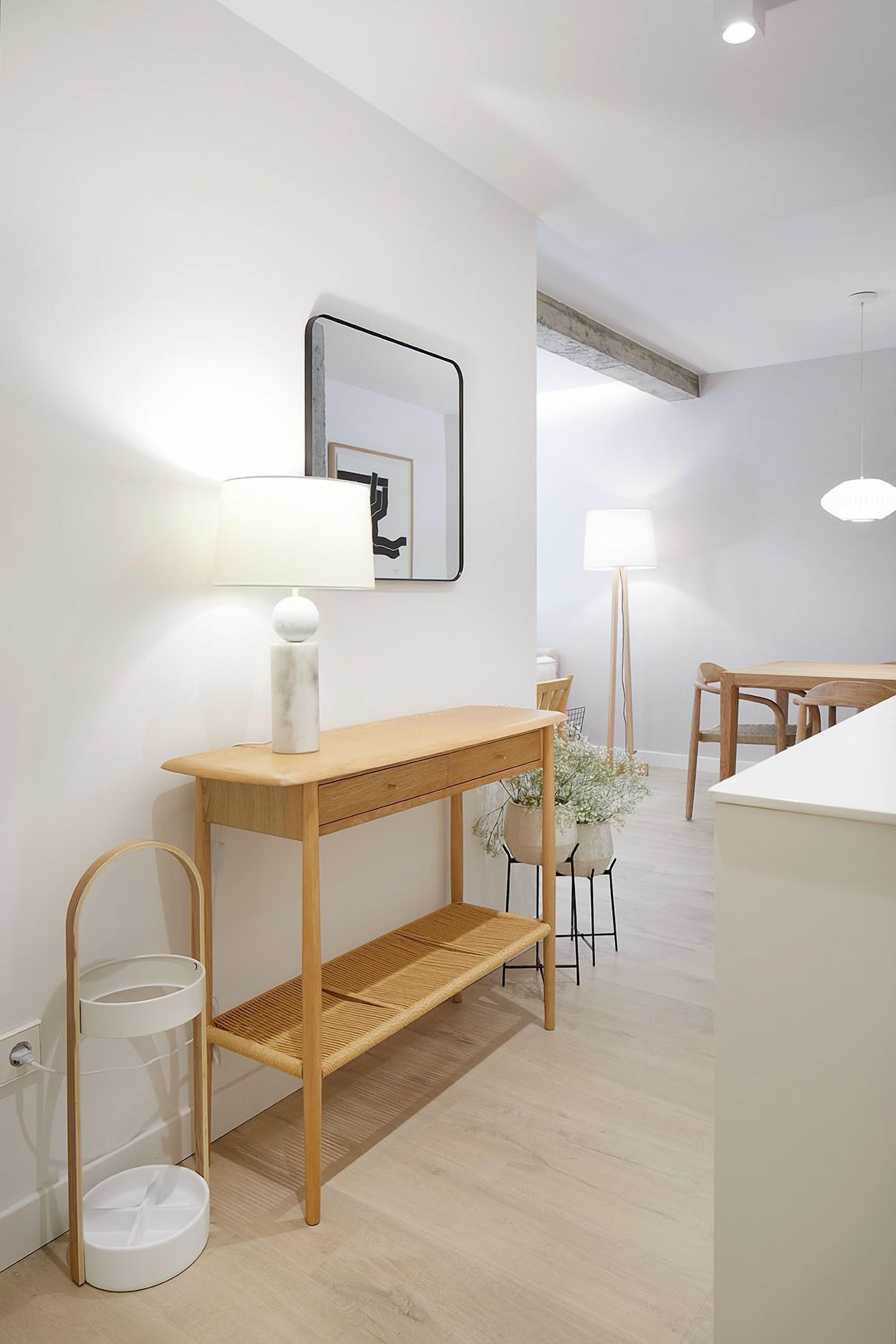 A modern, minimalist room with a wooden console table, a wall-mounted mirror, and a dining area with a wooden table and chairs.