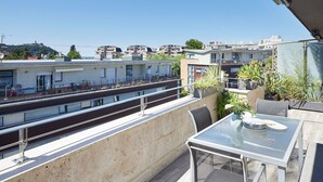 En balkon med et glasbord og stole, udsigt over et bybillede med bygninger og en klar himmel.