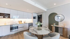 A modern kitchen with white cabinets, a built-in oven, and a dining area with a marble table and grey chairs.
