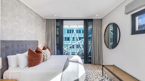 A modern hotel room with a large bed, a view of a building with a unique facade, and a circular mirror on the wall.