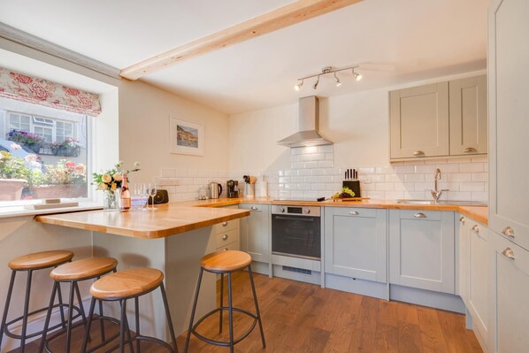 A kitchen with a wooden countertop, bar stools, a built-in oven, and a window with a view of flowers. - 2 Bed in Torquay (oc-sdmarg) (Torquay)