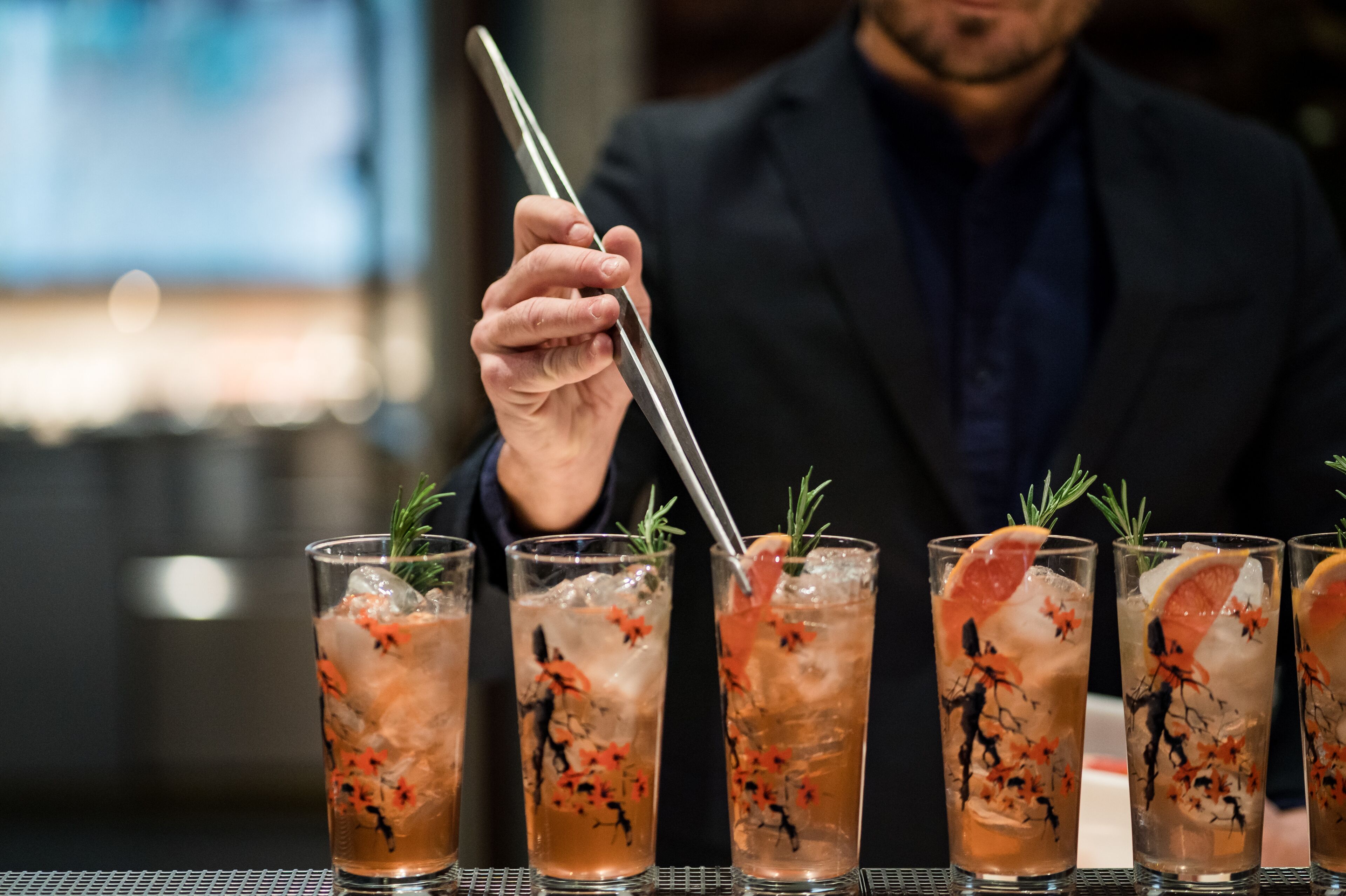 Un bar con varios vasos de cóctel, adornados con una rodaja de naranja y una ramita de romero.