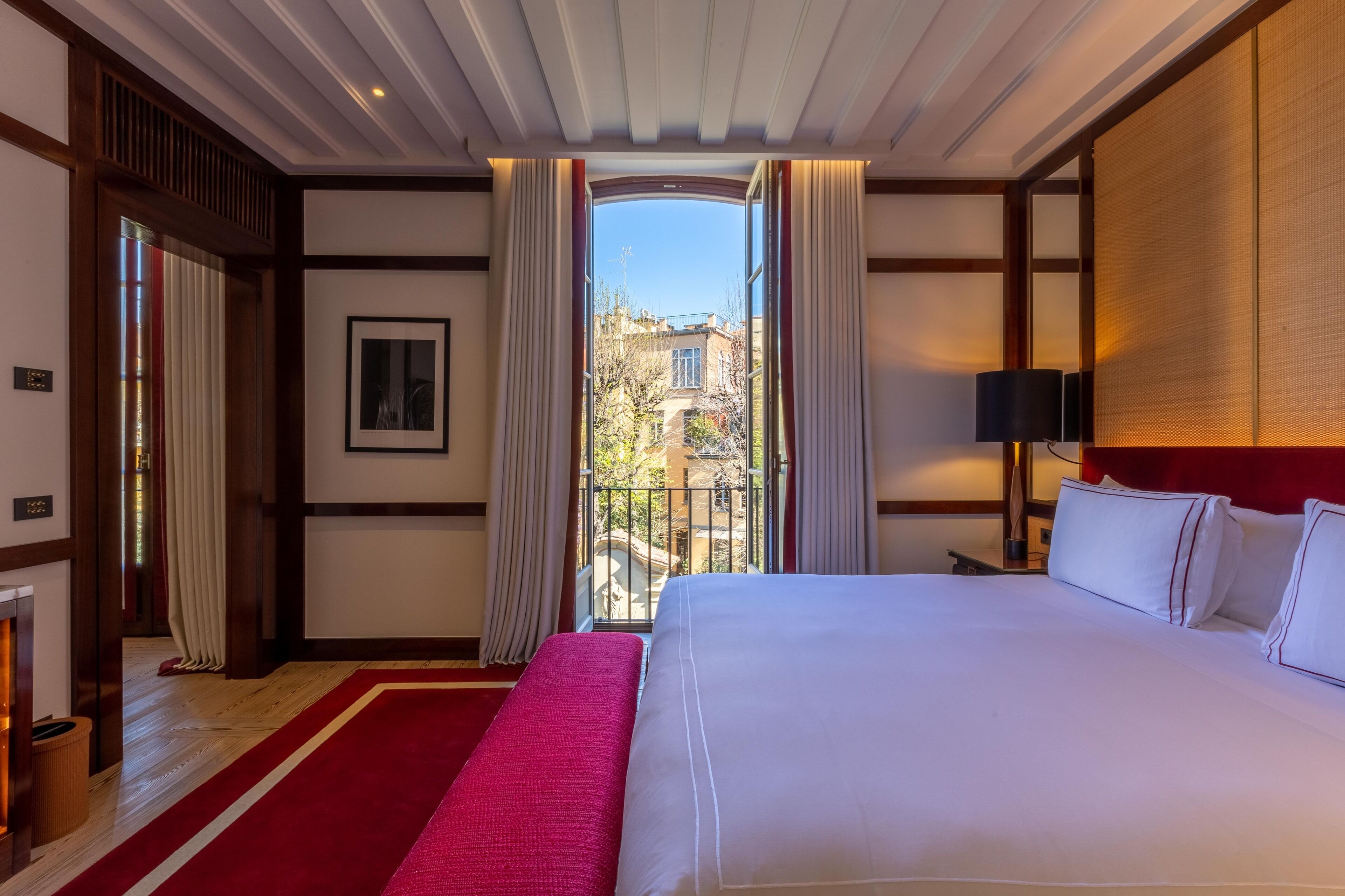 A hotel room with a large bed, a red carpet, a view of the outside, and a lamp on the nightstand.