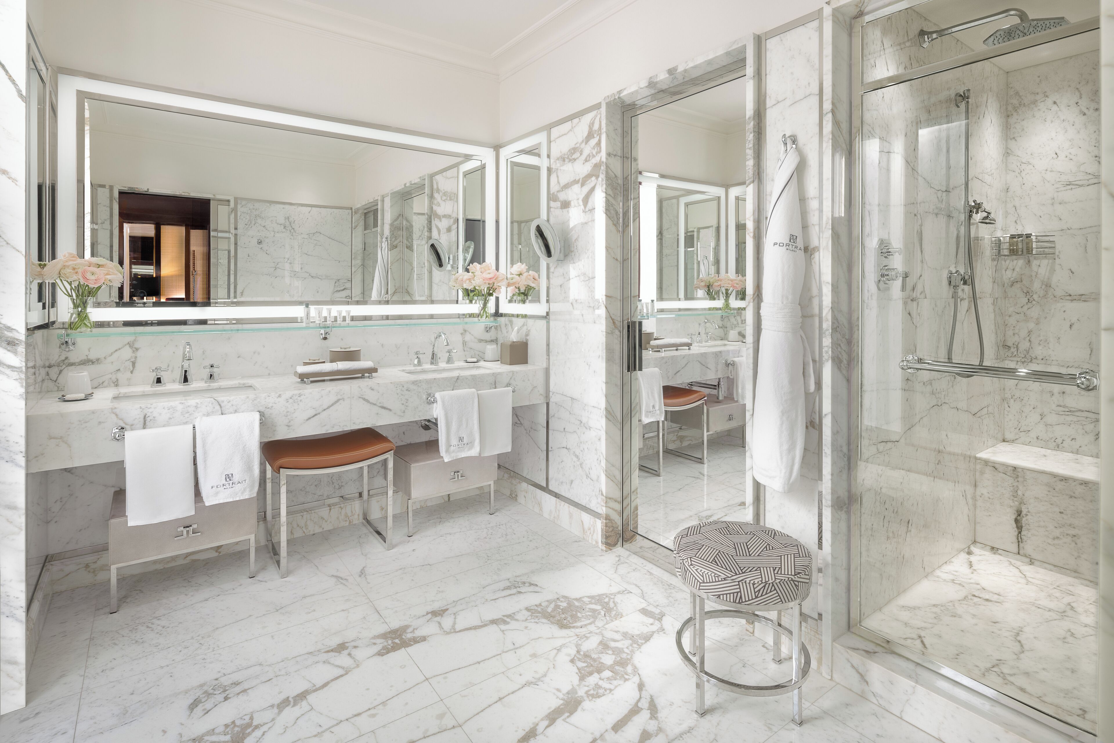 Un baño moderno con ducha envuelta en vidrio, suelo de mármol y un espejo grande sobre el lavabo.