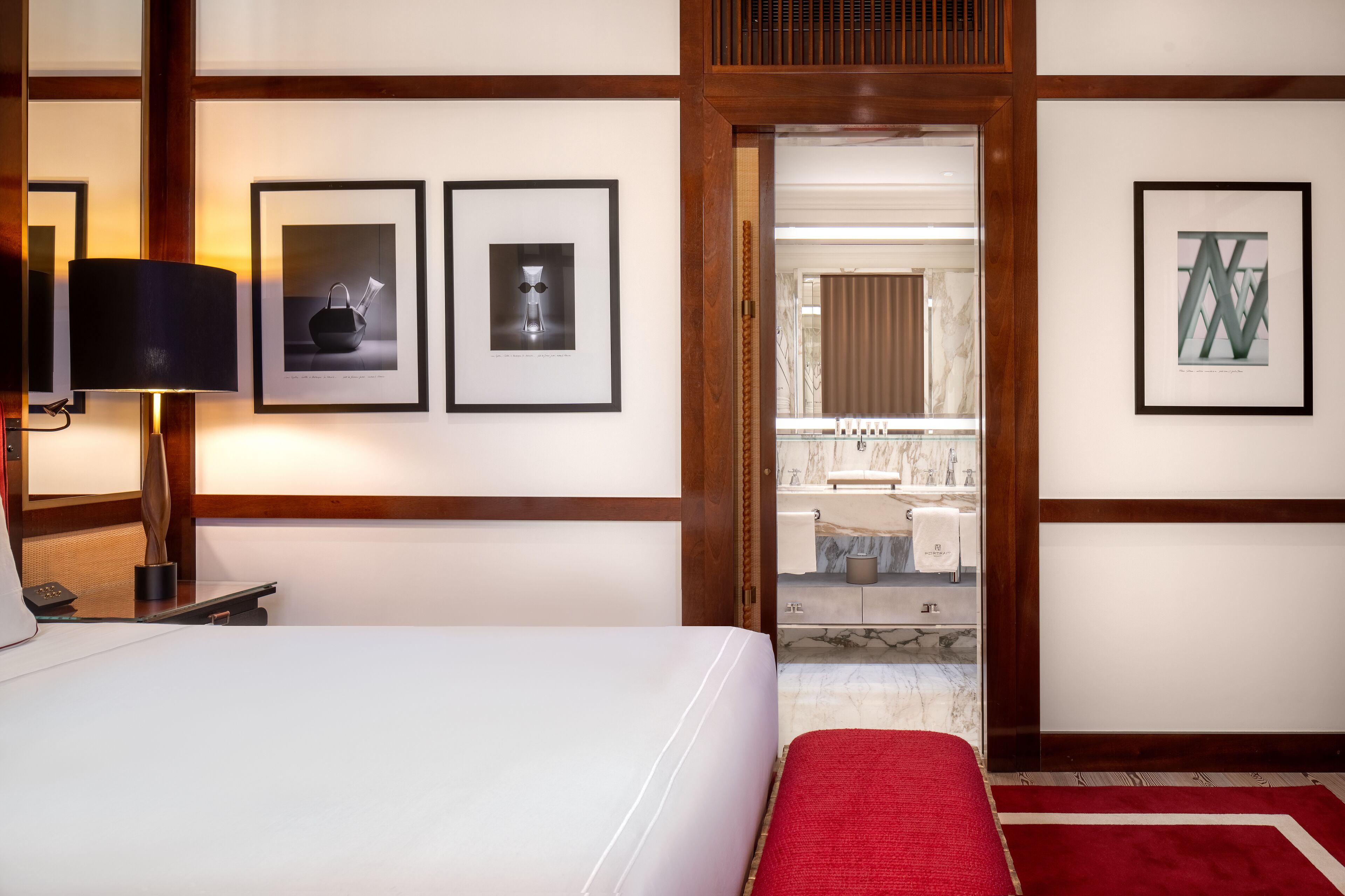 Ein Hotelzimmer mit einem Bett, einem roten Teppich, gerahmten Bildern an der Wand und einem durchgegangenen Tür erkennbaren Badezimmer.