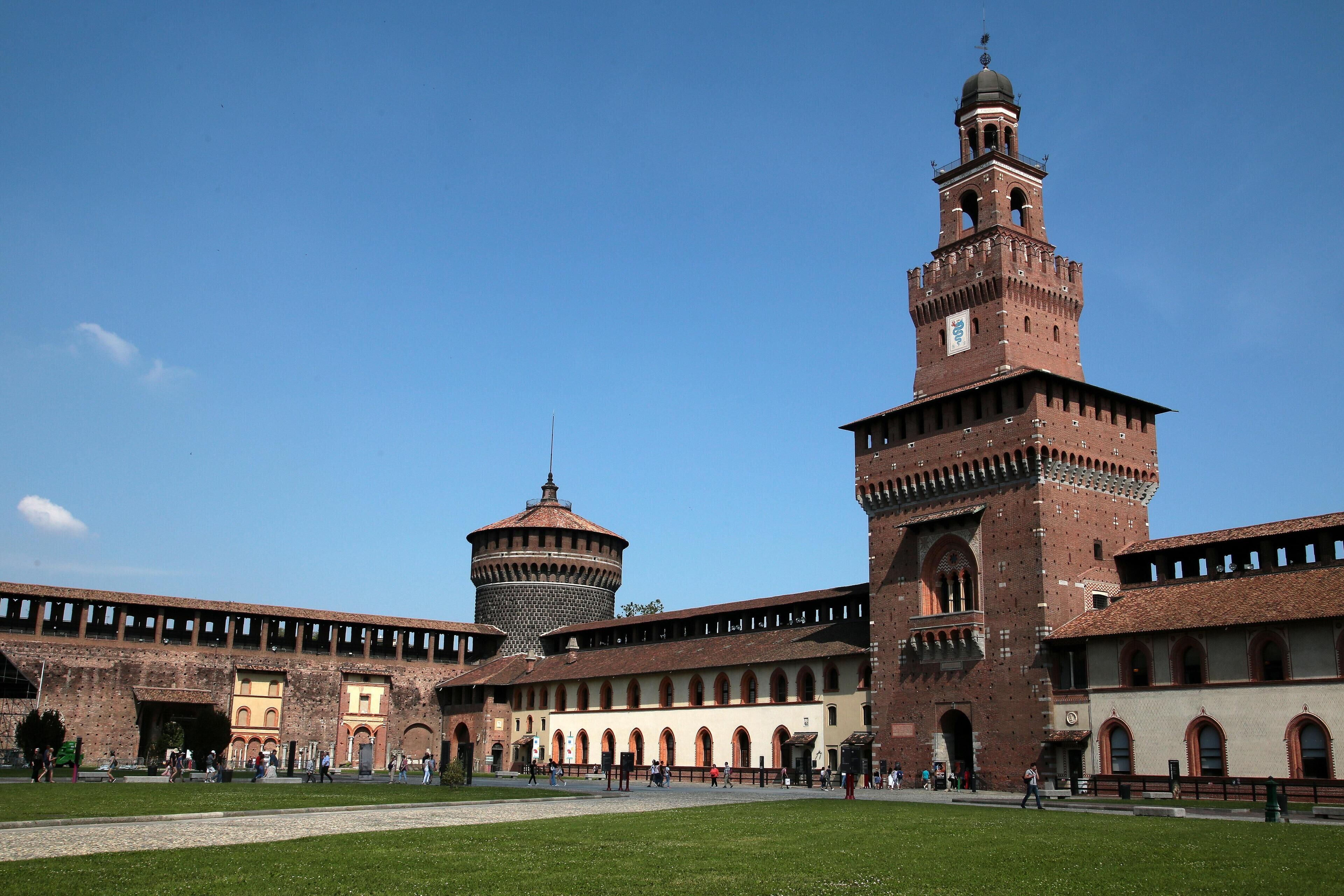 A historic building with a prominent tower and a round tower, surrounded by a courtyard with a grassy area and pathways.
