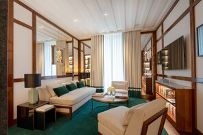 A hotel room with a sofa, a chair, a coffee table, a bookshelf, and a TV.