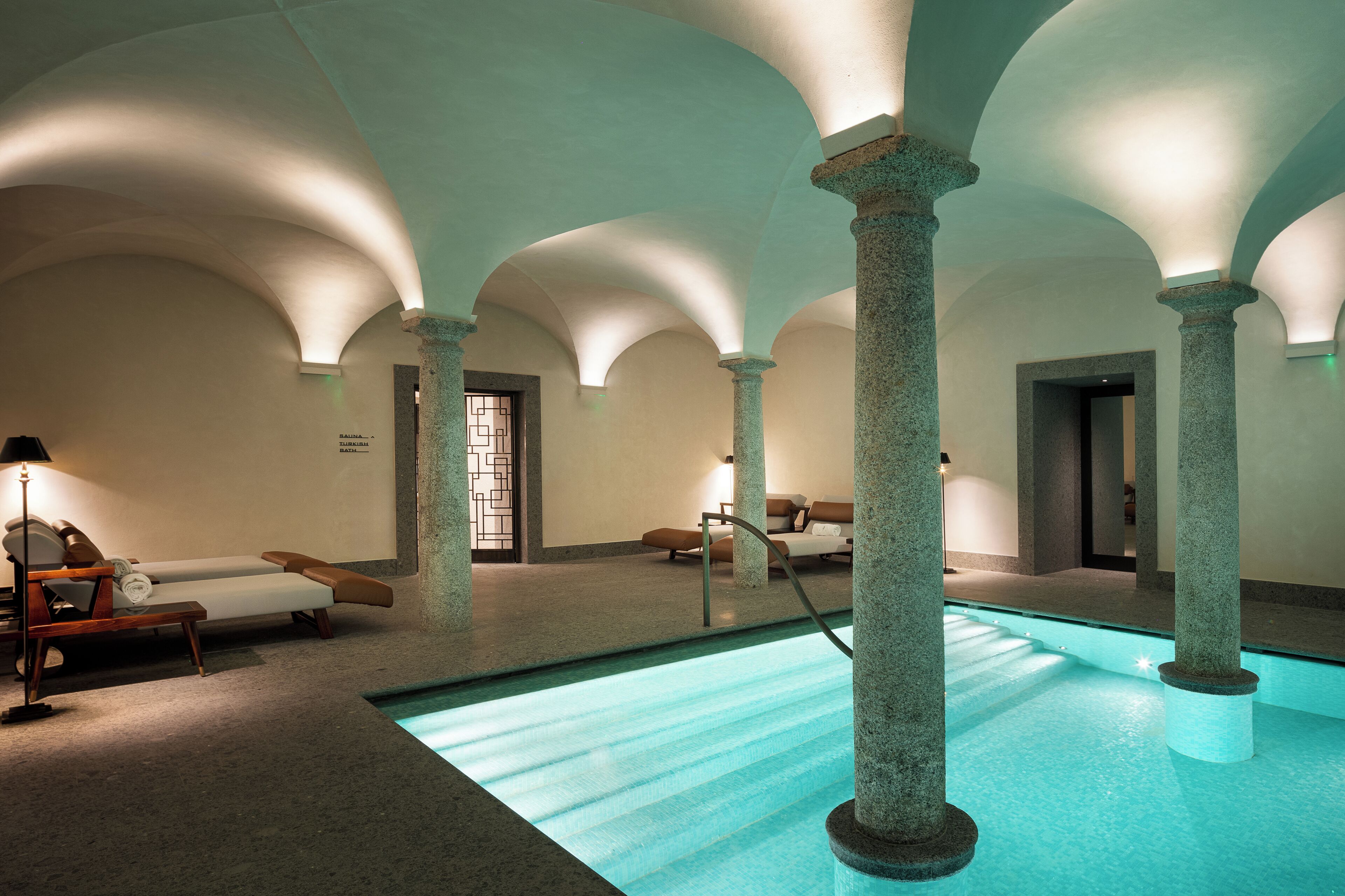 A spa area with a pool, lounge chairs, and stone columns.
