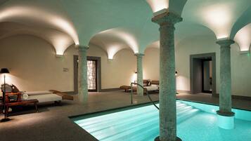 A spa area with a pool, lounge chairs, and stone columns.