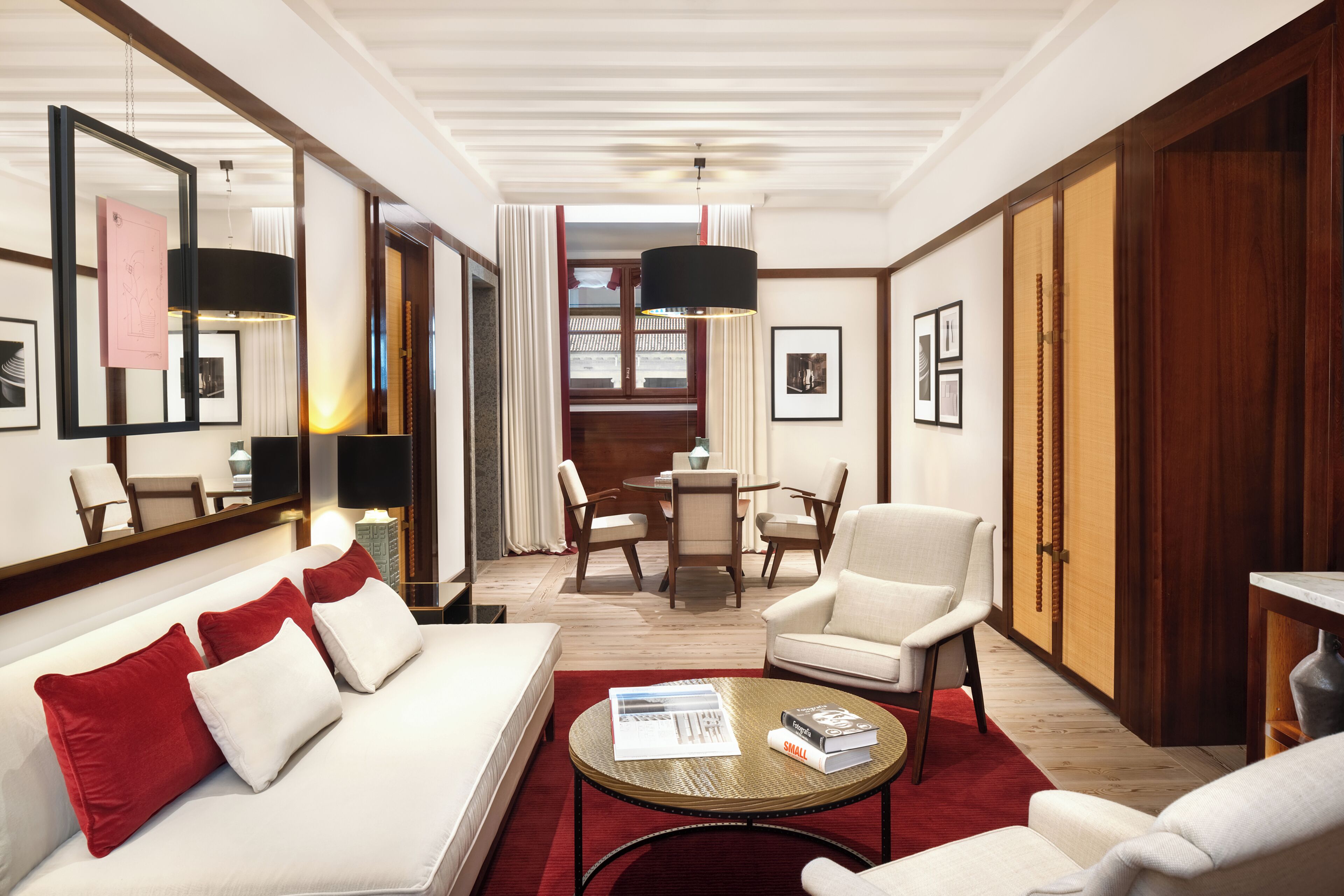 A modern hotel room with a sofa, armchairs, a dining table, and a large mirror.