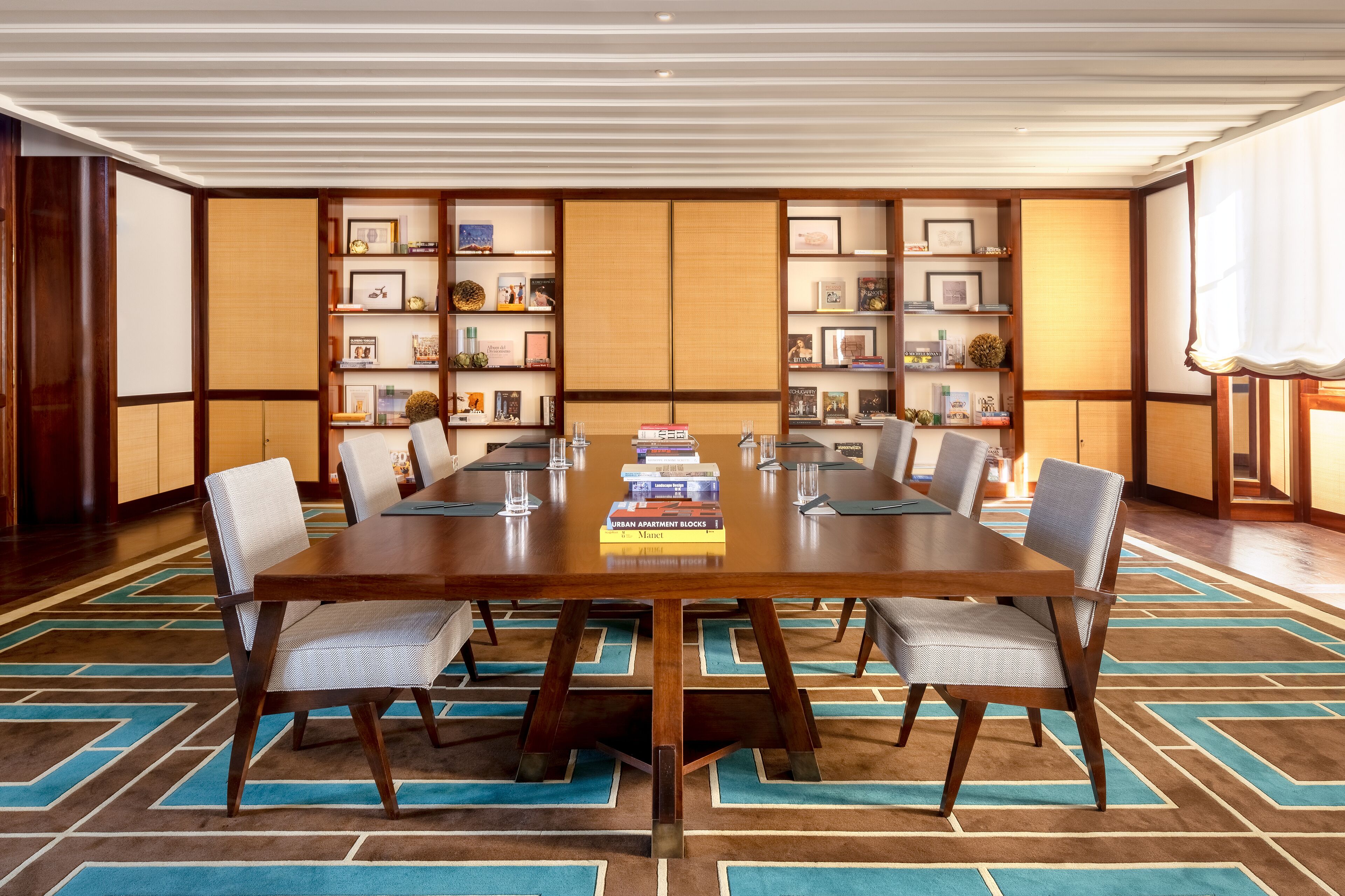 Une salle de conférence avec une grande table en bois, six chaises et une bibliothèque contenant des livres et des photos encadrées.
